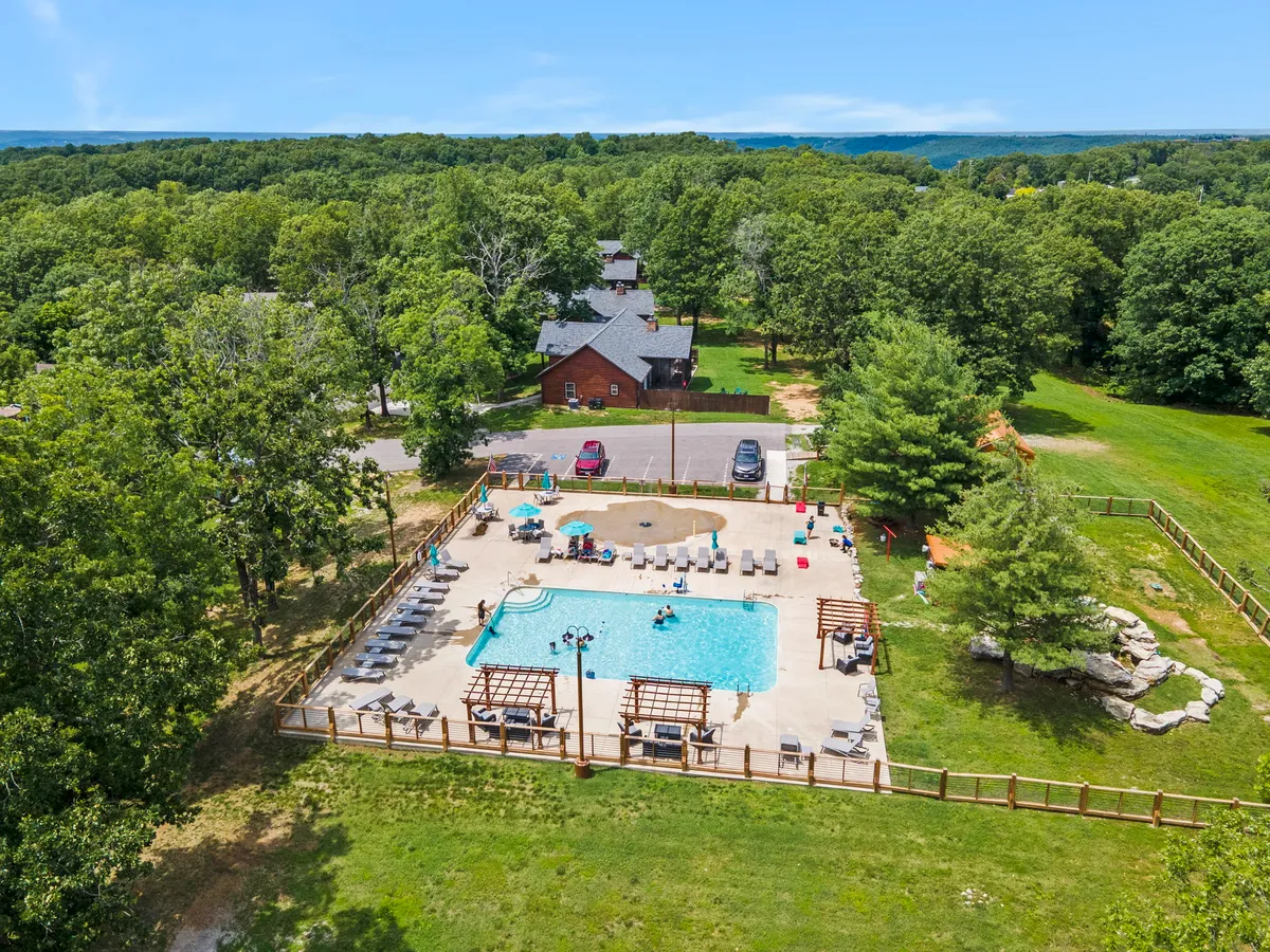 A sparkling swimming pool surrounded by lounge chairs, cabana structures, and mature trees. Children can be seen splashing and playing in the water as adults relax nearby, creating an atmosphere of cheerful relaxation and social connection.
