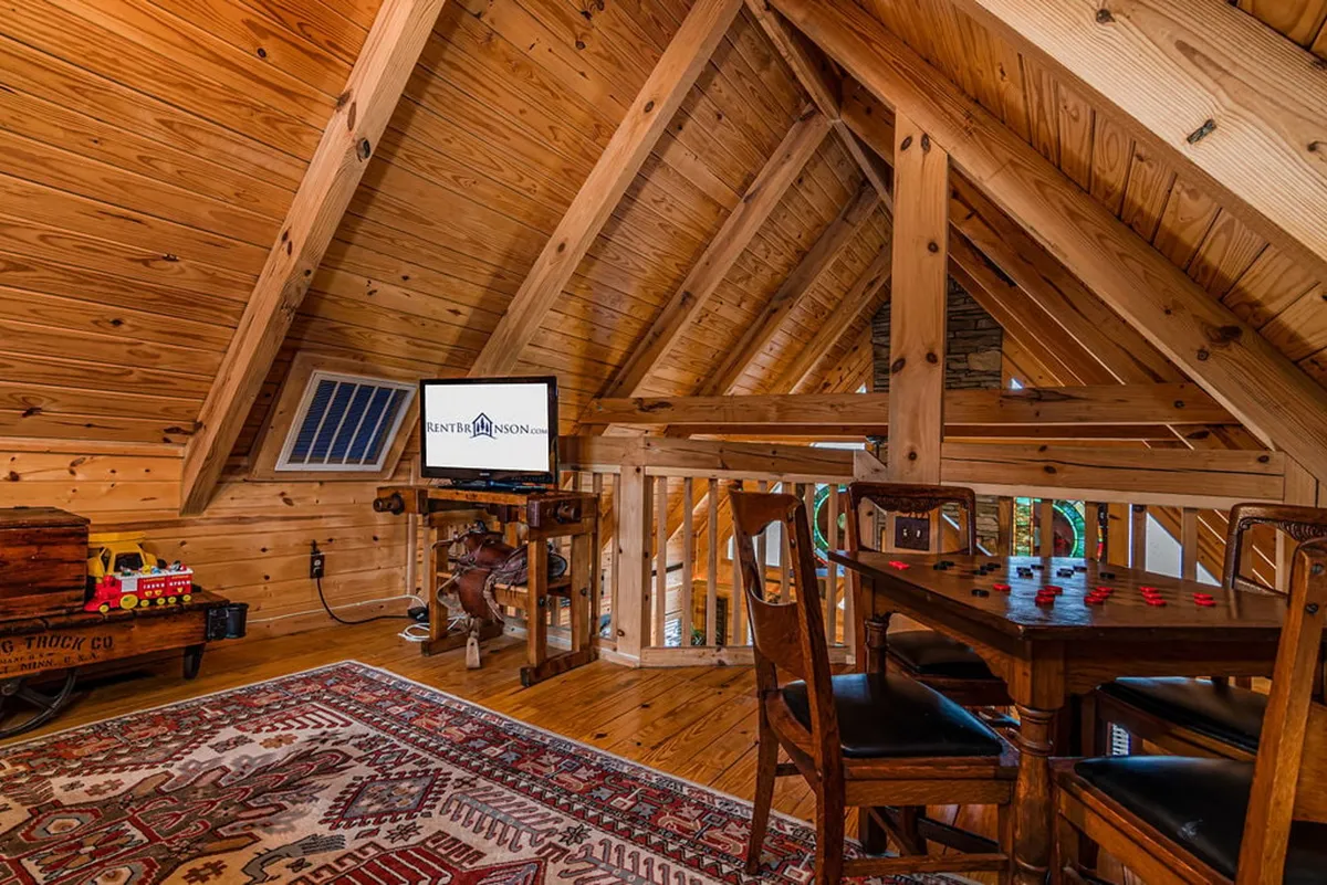 A spacious area with wooden beams, a dining or game table set atop a cozy rug, a television for entertainment, and natural light filtering in. The layout and furnishings create a setting perfect for board games, family gatherings, or game nights, echoing the section’s focus on fun and flexibility.