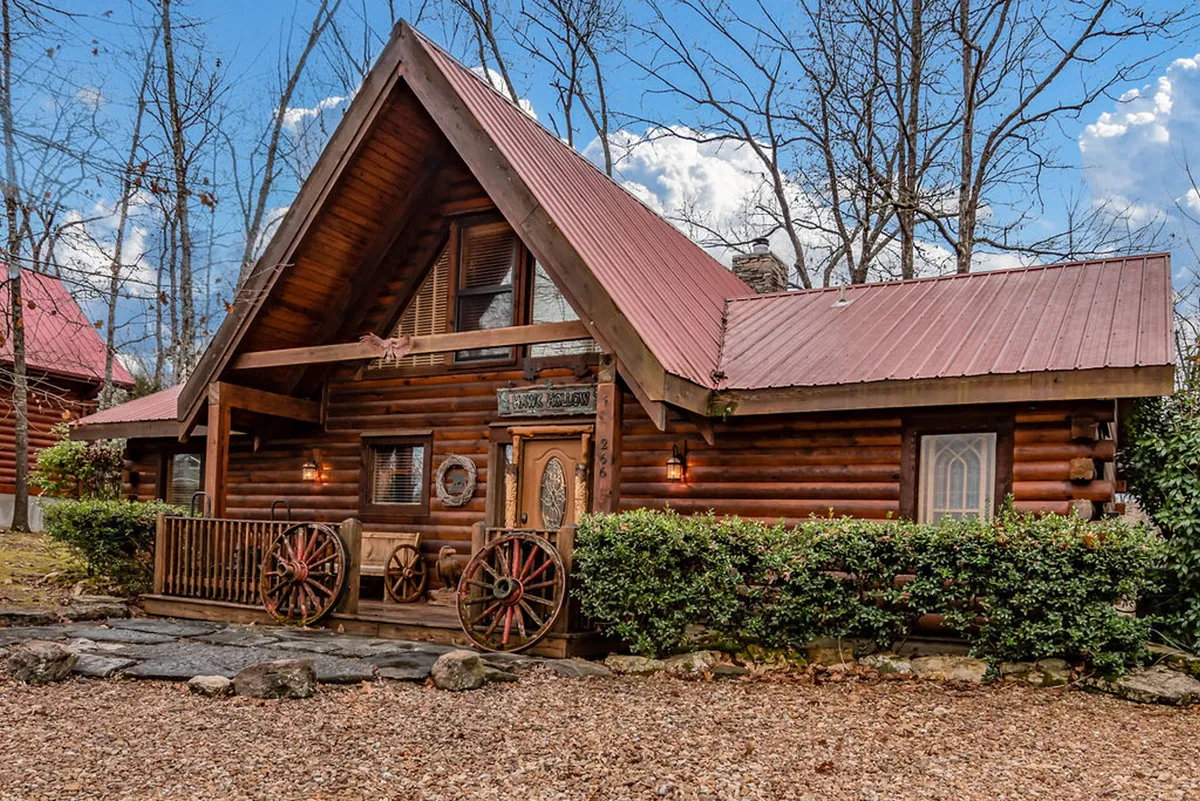 This image features a classic log cabin structure with decorative wagon wheels and a cozy front porch surrounded by nature. The scene hints at an inviting, communal space ideal for small-group relaxation and gatherings, and the porch is set up for unwinding while enjoying beautiful sunset views.