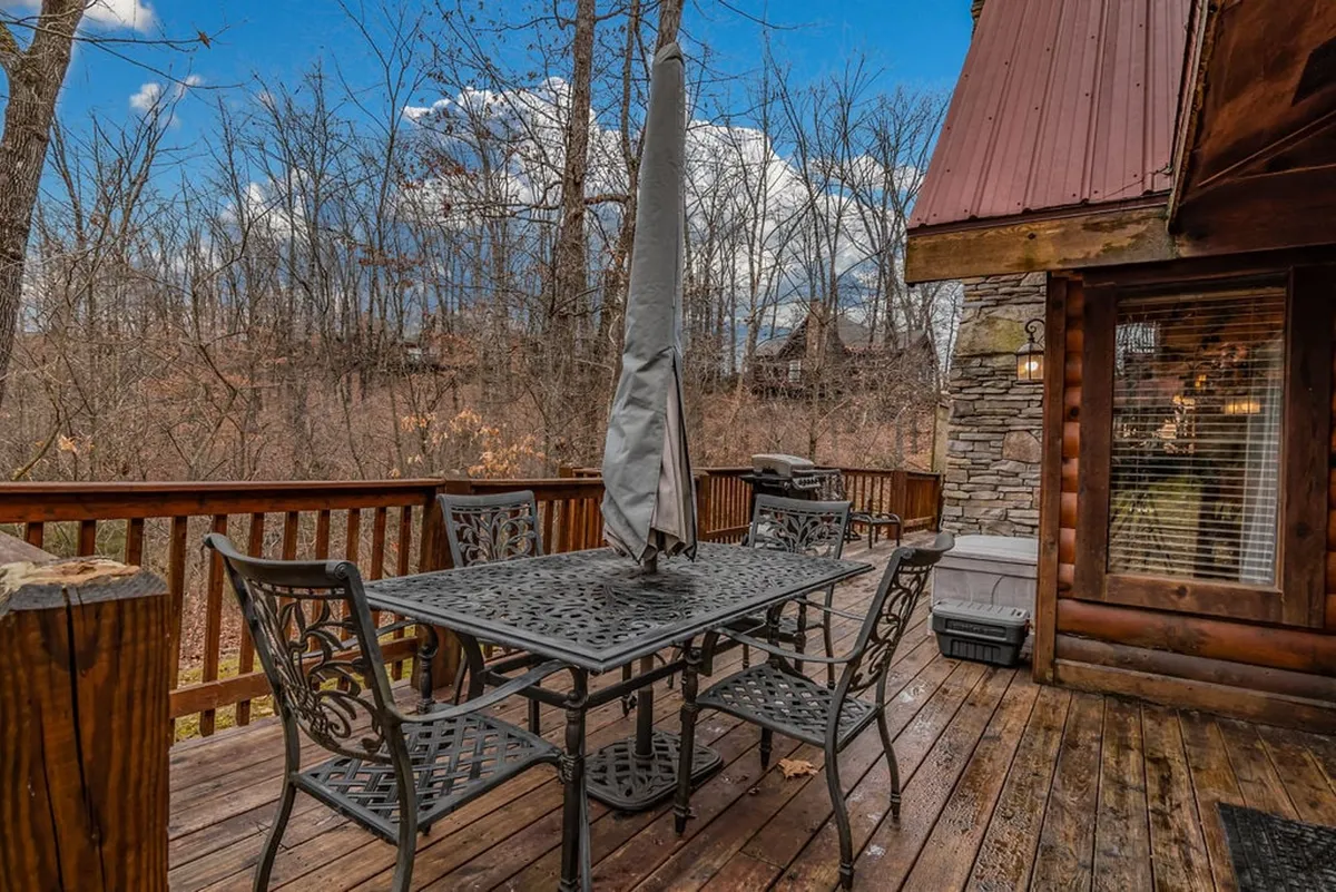 A wooden deck set among the trees offers a metal patio table with an umbrella, perfect for outdoor dining or morning coffee. The surrounding woodland provides a peaceful, natural backdrop, enhancing the sense of serenity and privacy.