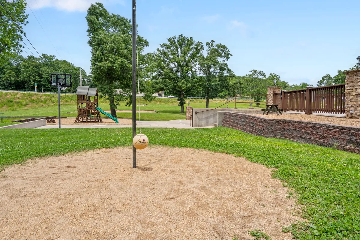 This lively outdoor scene captures a vibrant play area featuring volleyball poles, a basketball hoop, a children's play structure, and a picnic area. Families and children are engaged in games and socializing, highlighting a strong sense of community and fun.