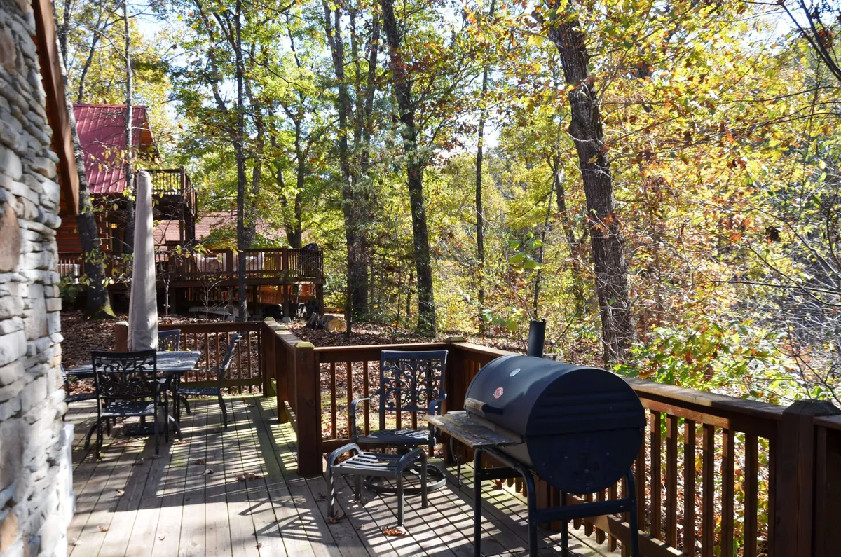 A cozy deck with a grill, outdoor dining furniture, and surrounding woodland. The seating area looks inviting for al fresco dining or relaxed gatherings as daylight fades.