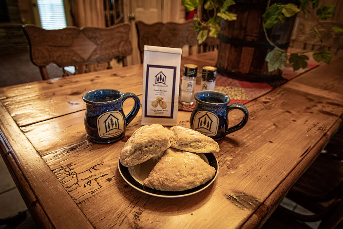 A rustic wooden table set with ceramic mugs and freshly baked scones, surrounded by warm wood paneling. The scene conjures a feeling of cozy togetherness—an ideal setting for sharing snacks during a board game marathon or enjoying quiet moments after a day of fun.