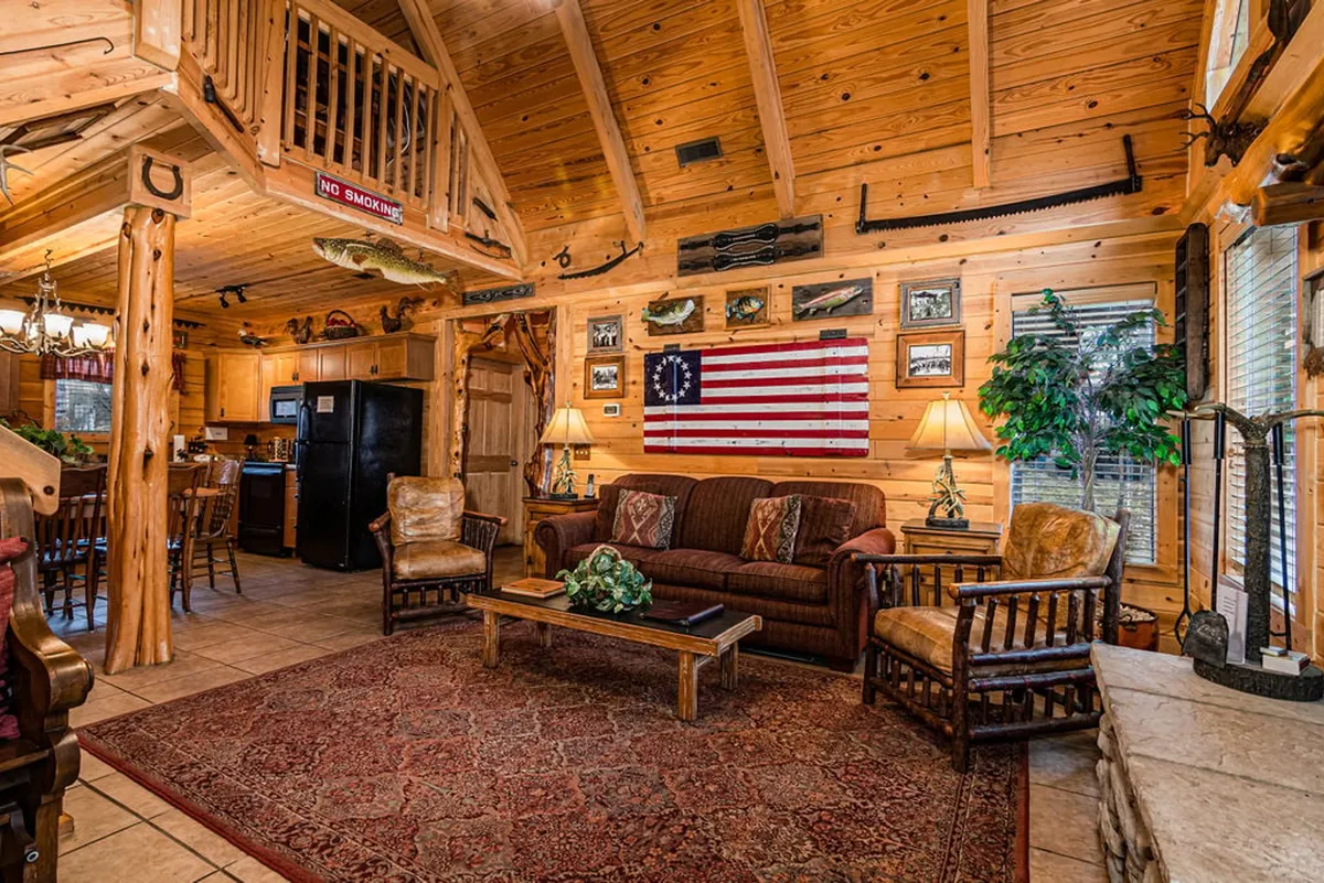 A cozy great room anchored by a plush sofa and coffee table, accented with wooden beams, an American flag, and decorative wall-mounted fish. The welcoming setting invites relaxation, socializing, and games, with rustic charm evident in every detail.