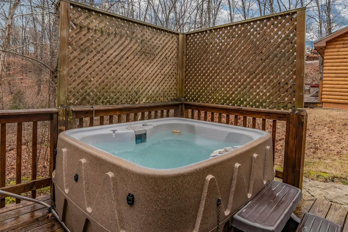 A serene outdoor scene with a private hot tub nestled among trees behind a wooden lattice fence. The setting is tranquil and inviting, perfect for unwinding after a day of adventure and group activities.